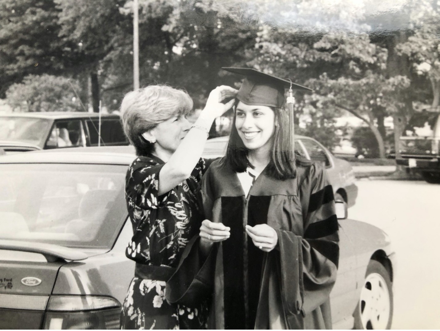 Black and white photo of Monika in her graduation robe and a woman adjusting her cap