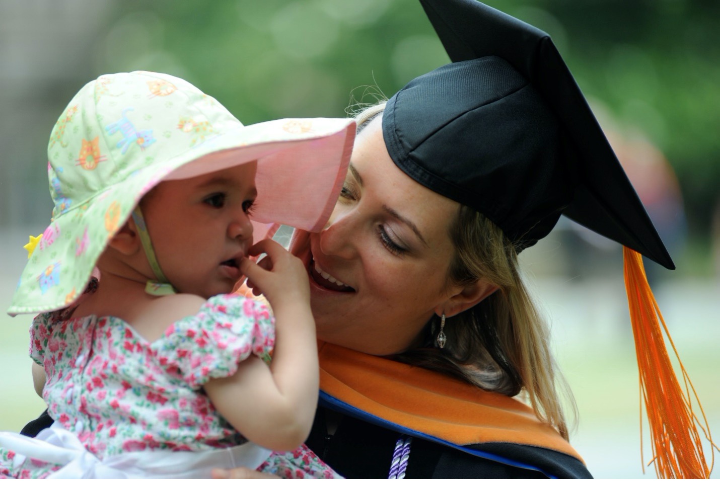 Elizabeth Rodriguez in graduation robe holding a child